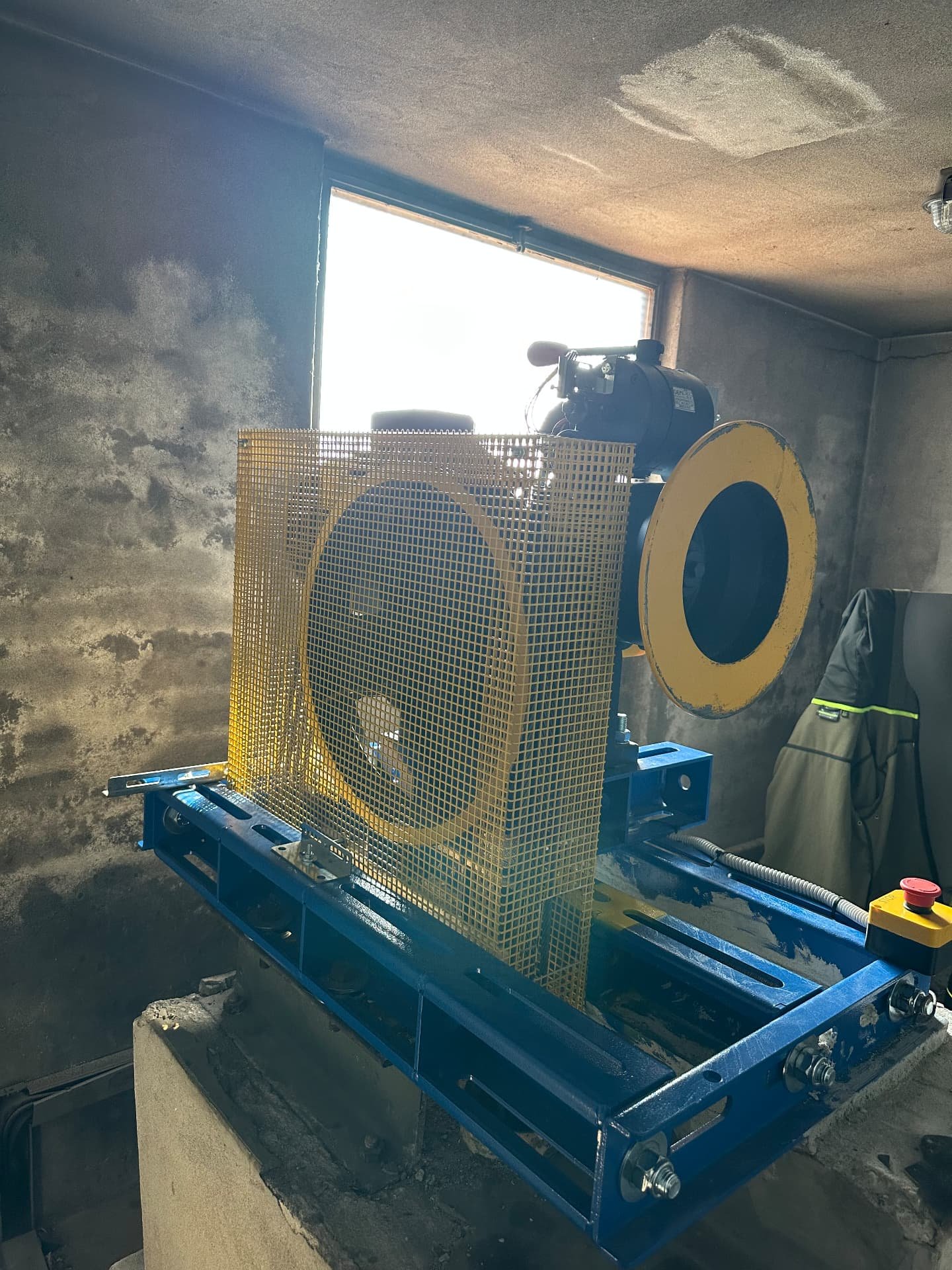 Nuovo argano gearless con telaio blu, puleggia gialla e griglia di protezione installato nel locale macchine