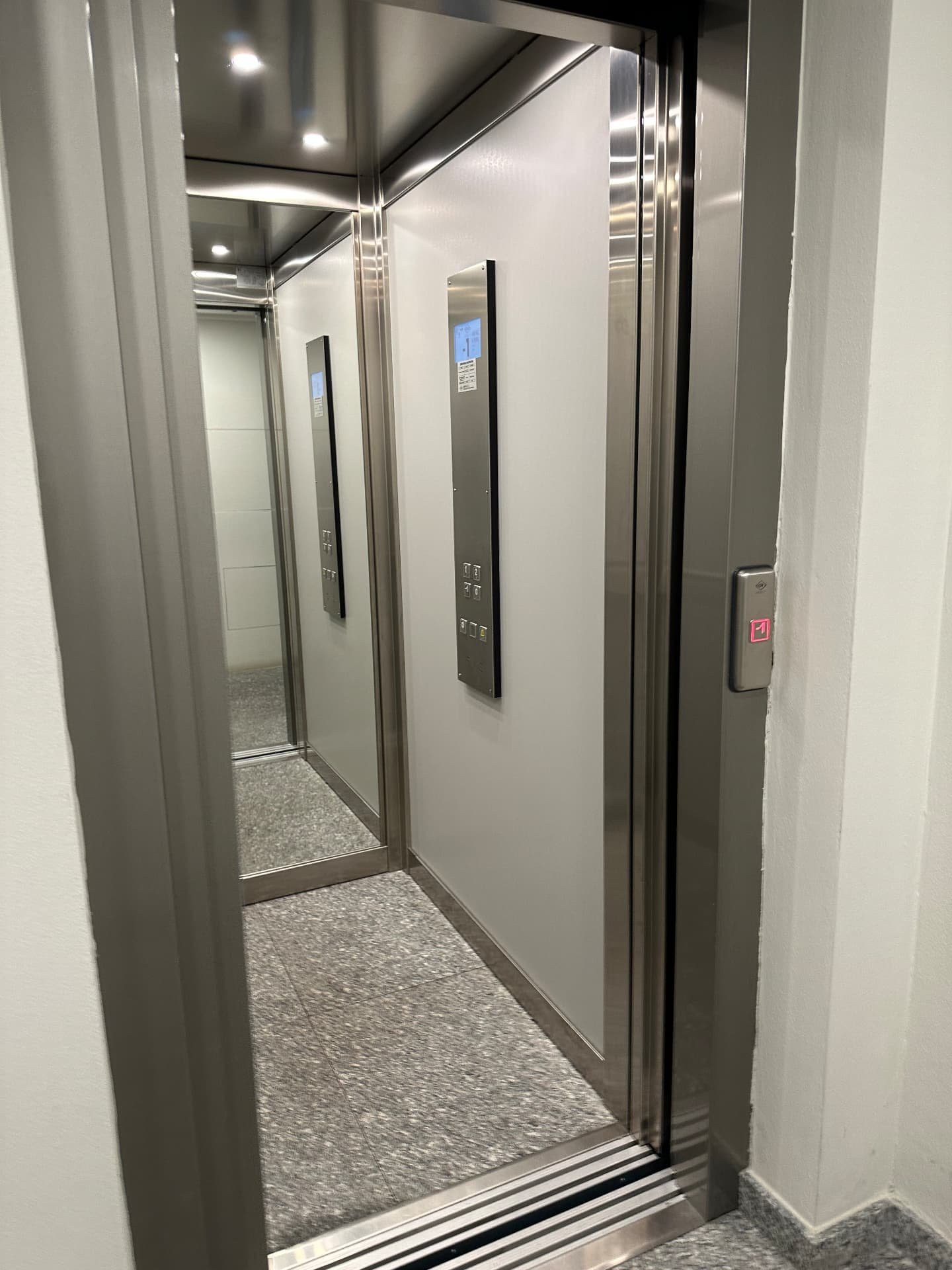 Cabina ascensore moderna con pareti chiare, specchio, pulsantiera con display e faretti LED