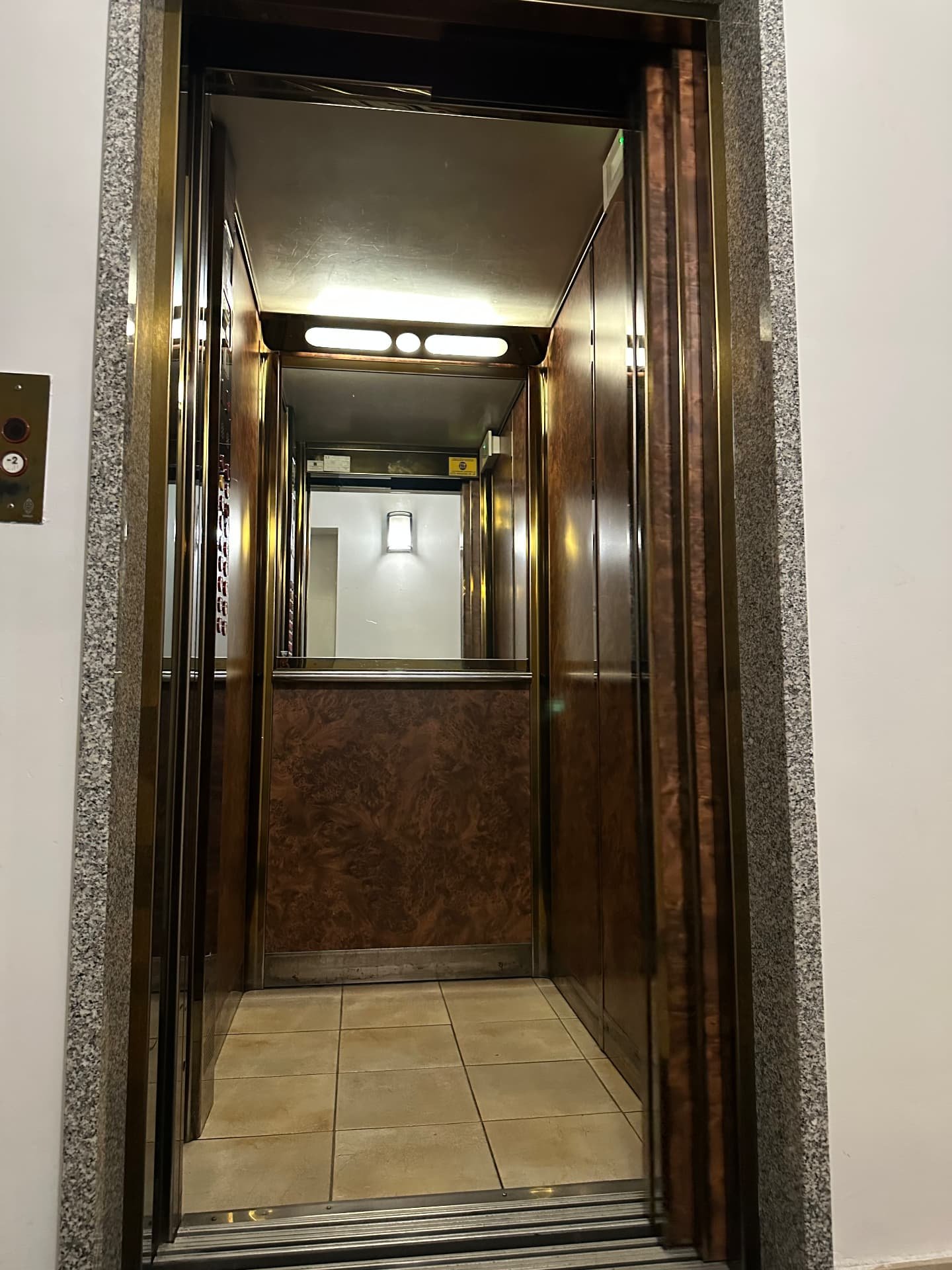 Cabina ascensore con rivestimento effetto legno, specchio e pavimento piastrellato